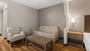 A modern hotel room with a sofa, armchair, wooden coffee table, and a bedside table with a lamp. - Red Roof Inn & Suites Newnan (Newnan)