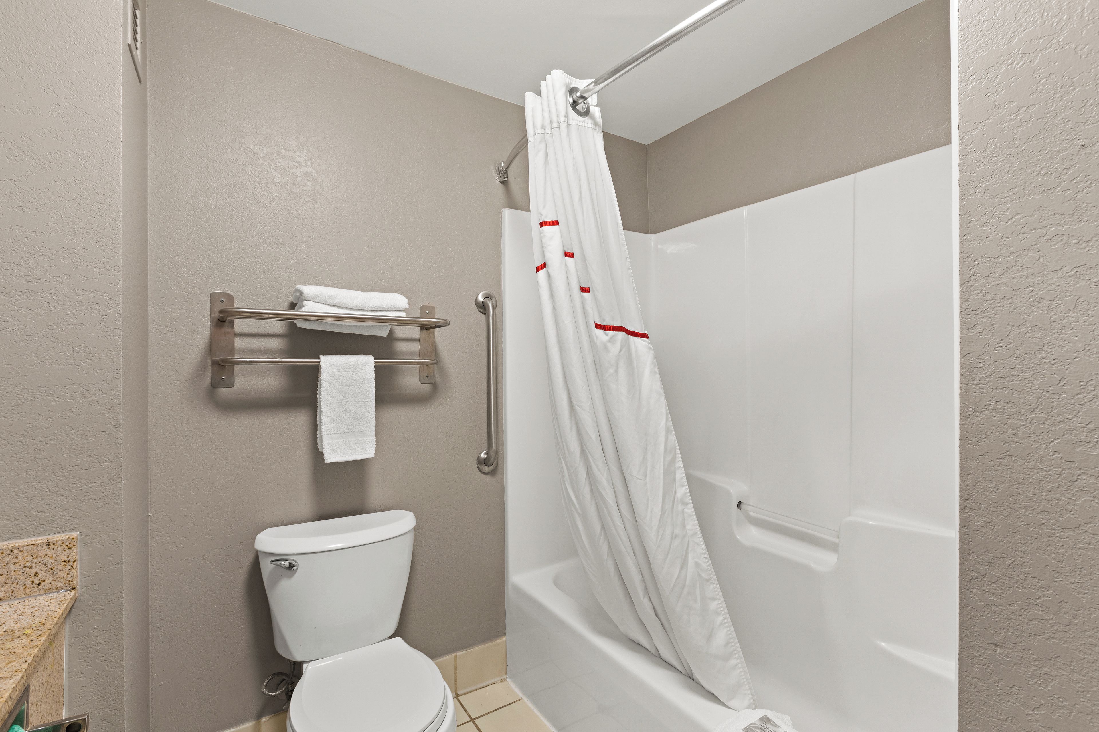 A bathroom with a toilet, a shower with a white curtain, and a towel rack with a towel.