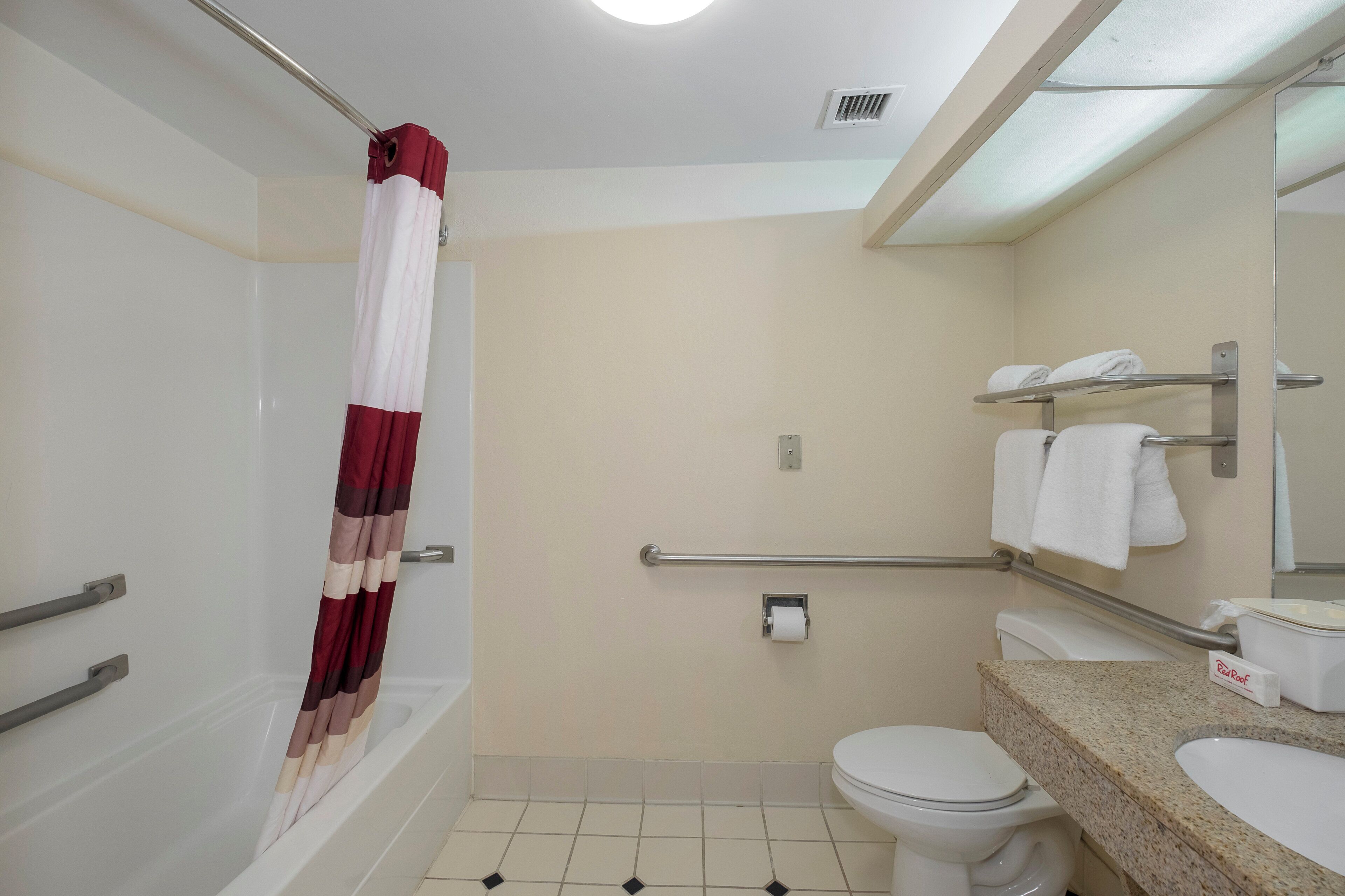 Une salle de bain équipée d’une baignoire, de toilettes et d’un lavabo. On y trouve également des barres d’appui et un porte-serviettes.