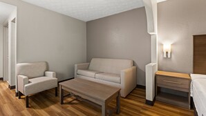 A modern hotel room with a wooden floor, a sofa, a chair, a small table, and a nightstand with a lamp.