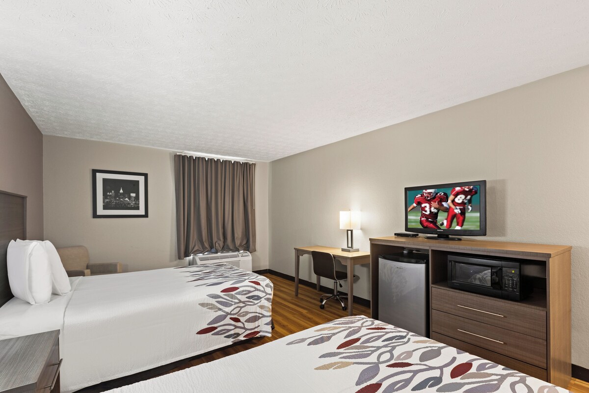 A hotel room with two beds, a desk, a television, and a microwave.