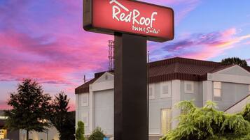 Un letrero de Red Roof Inn & Suites con un edificio moderno al fondo.