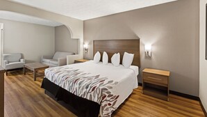 A hotel room with a large bed, a sitting area with a chair and a table, and a wooden floor. - Red Roof Inn & Suites Newnan (Newnan)