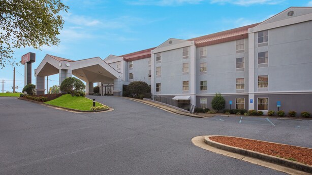 A modern hotel with a covered entrance, a parking lot, and a landscaped area with a small hill. - Red Roof Inn & Suites Newnan (Newnan)