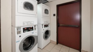 A laundry room with stacked washers and dryers, a door, and a sign indicating the location of the stairs. - Red Roof Inn & Suites Newnan (Newnan)
