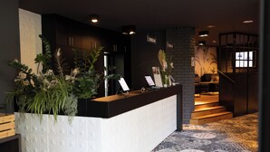 Zona de recepción con mostrador, plantas y una escalera que sube a otro nivel.
