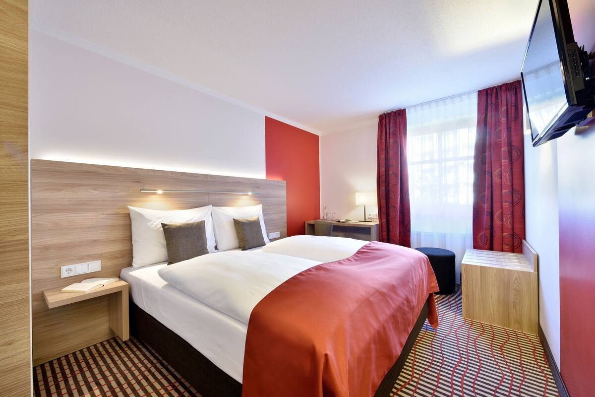 Ein Hotelzimmer mit Bett, Nachttischen, Fernseher und einem Fenster mit Vorhängen.