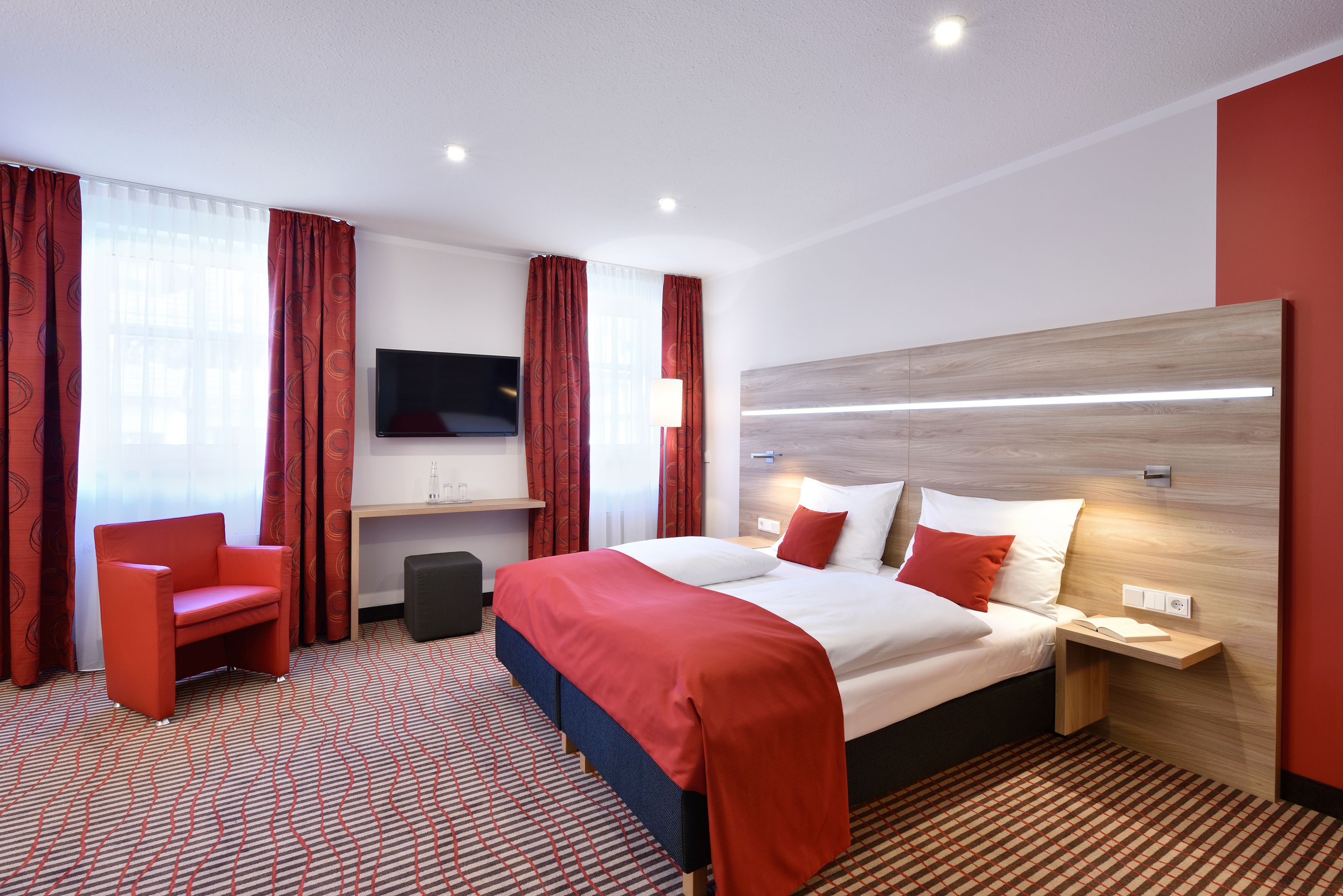 A hotel room with a bed, a TV, a desk, and a chair.