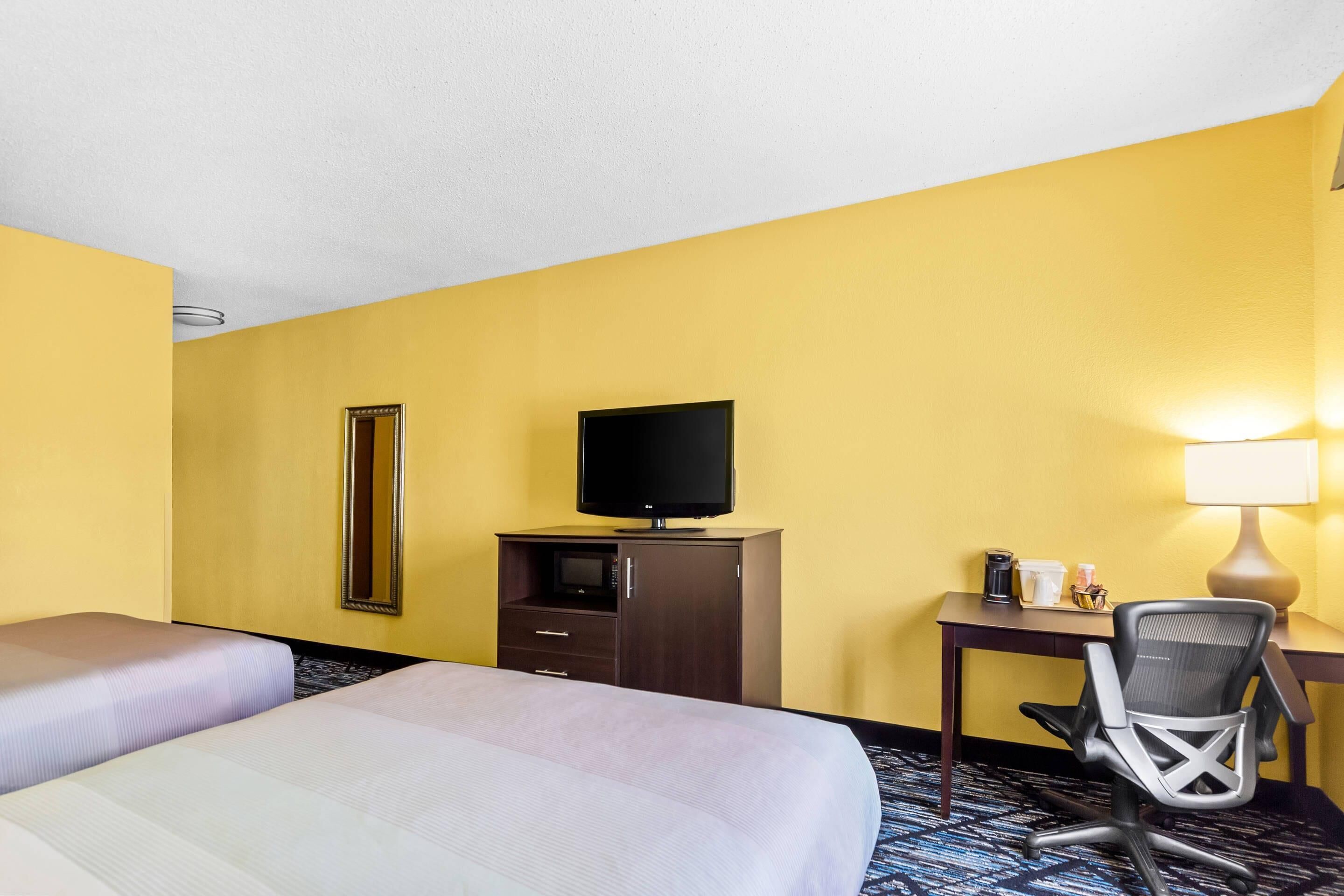 Una camera d'albergo con due letti, una scrivania con una sedia, una televisione, uno specchio e una lampada.