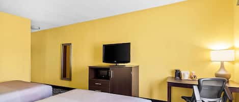 A hotel room with two beds, a desk with a chair, a television, a mirror, and a lamp.