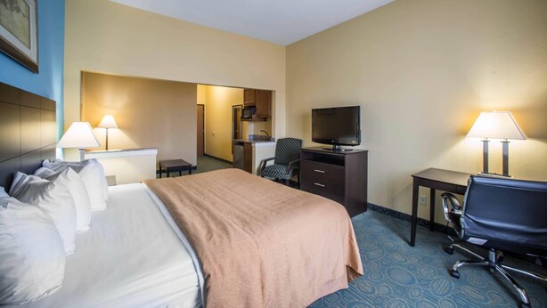Ein Hotelzimmer mit Bett, Schreibtisch, Stuhl, Fernseher und einer Küchenzeile.