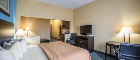 A hotel room with a bed, desk, chair, television, and a kitchenette.