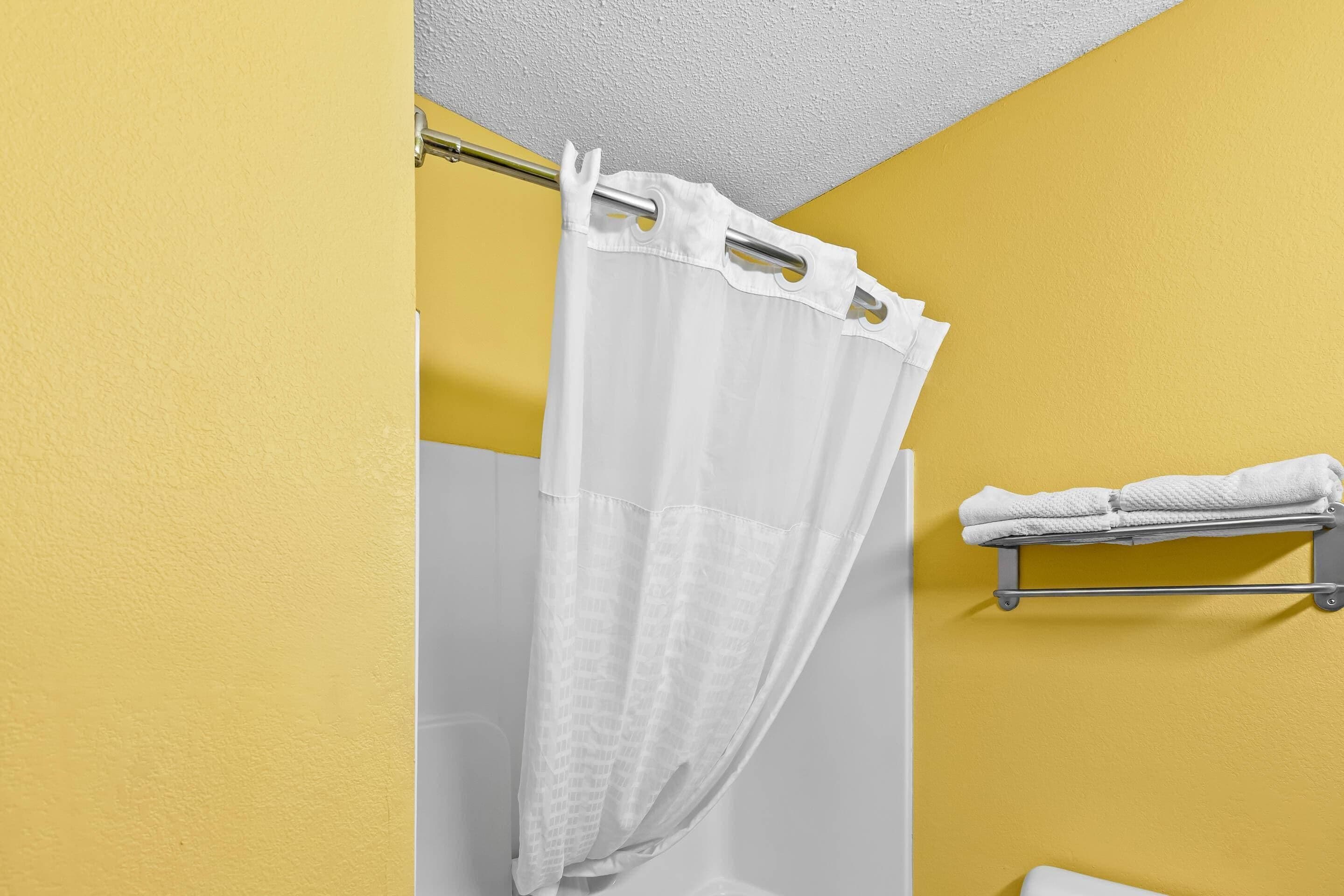 A bathroom with a shower curtain, a towel rack with towels, and a yellow wall.
