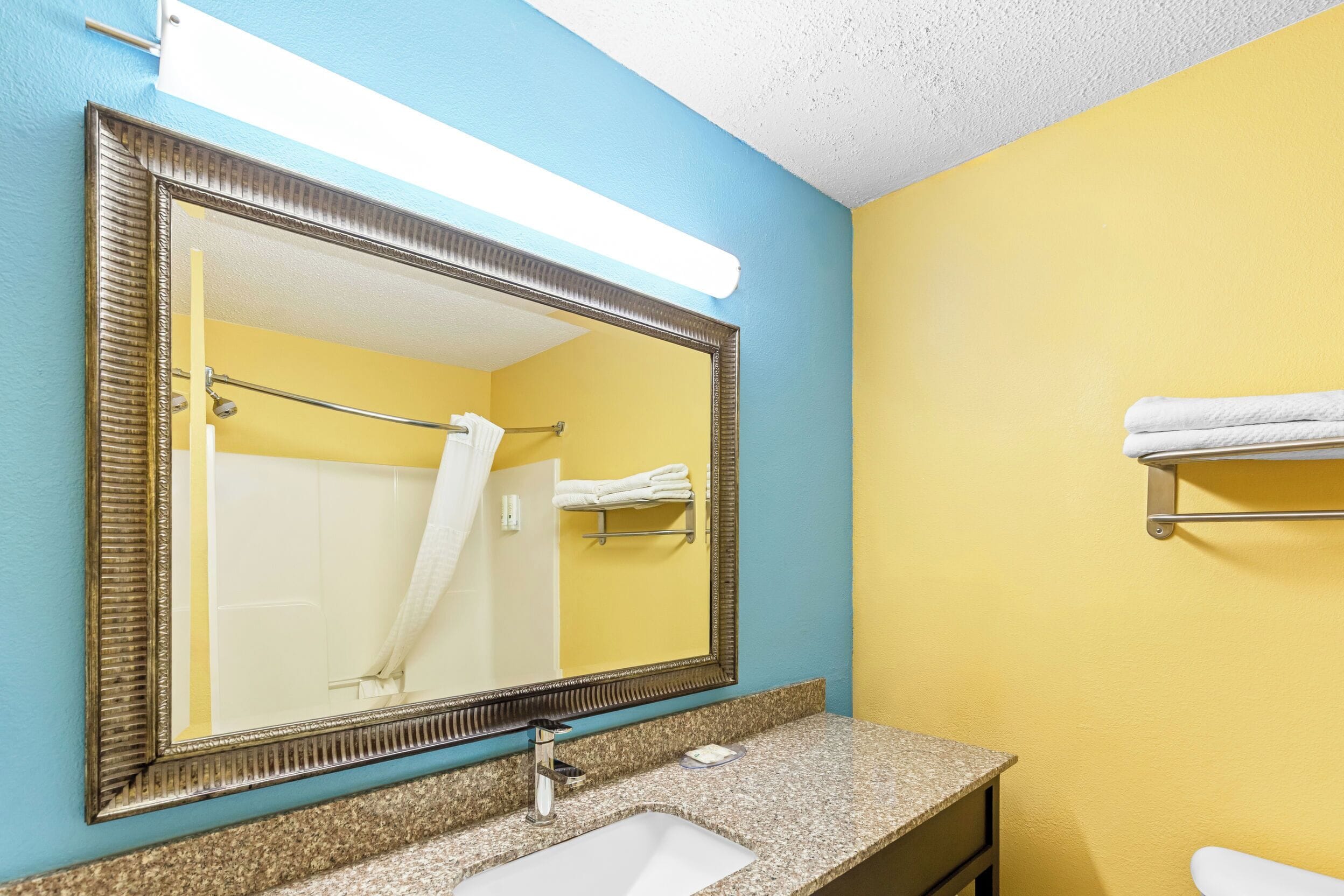 A bathroom with a large mirror, a sink, and a towel rack.