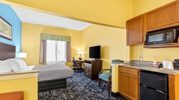 A hotel room with a bed, desk, chair, kitchenette, and a television.