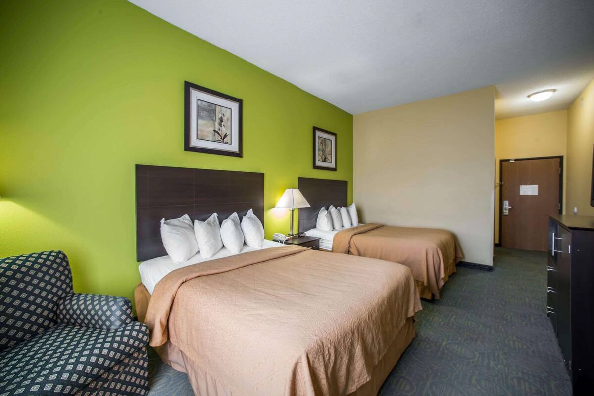 Habitación de hotel con dos camas, un escritorio, una lámpara y un aparador.