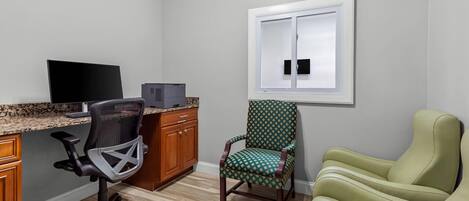 Una habitación con escritorio, computadora, silla de oficina, sillón estampado y un sofá.