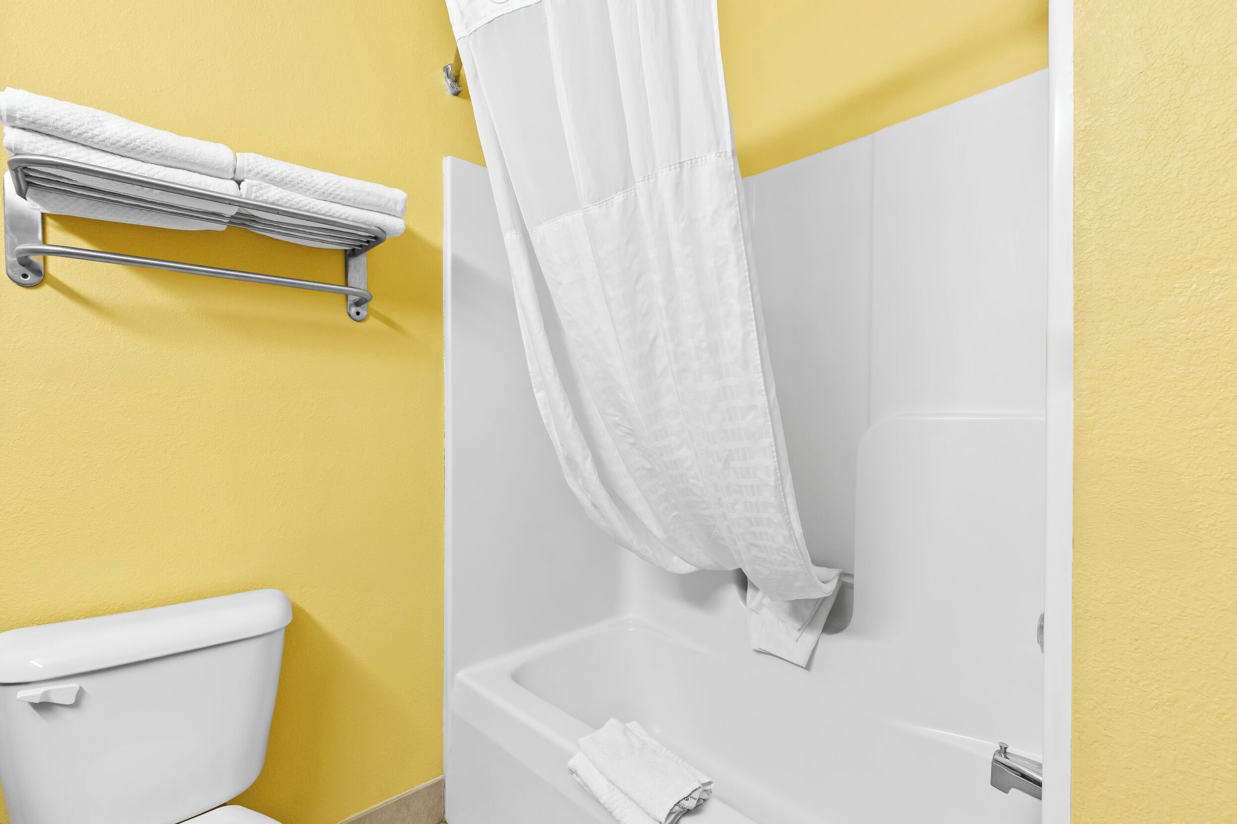 A bathroom with a white toilet, a bathtub, and a towel rack with folded towels.