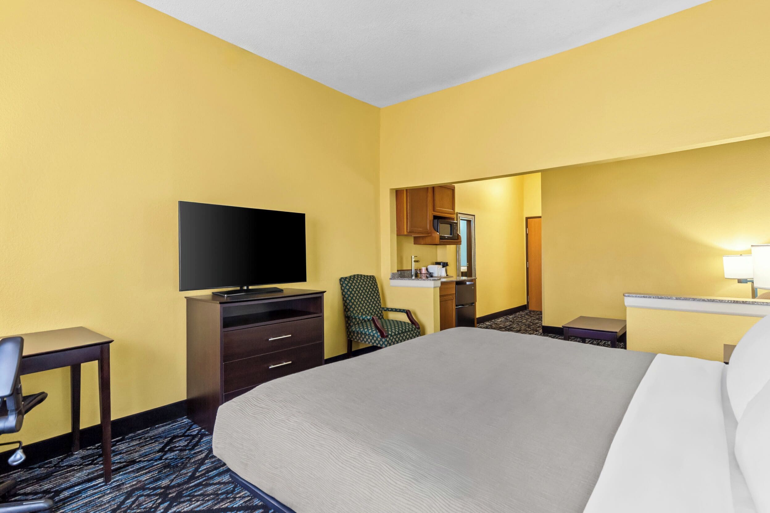 Habitación de hotel con cama, escritorio, televisión, silla y kitchenette.