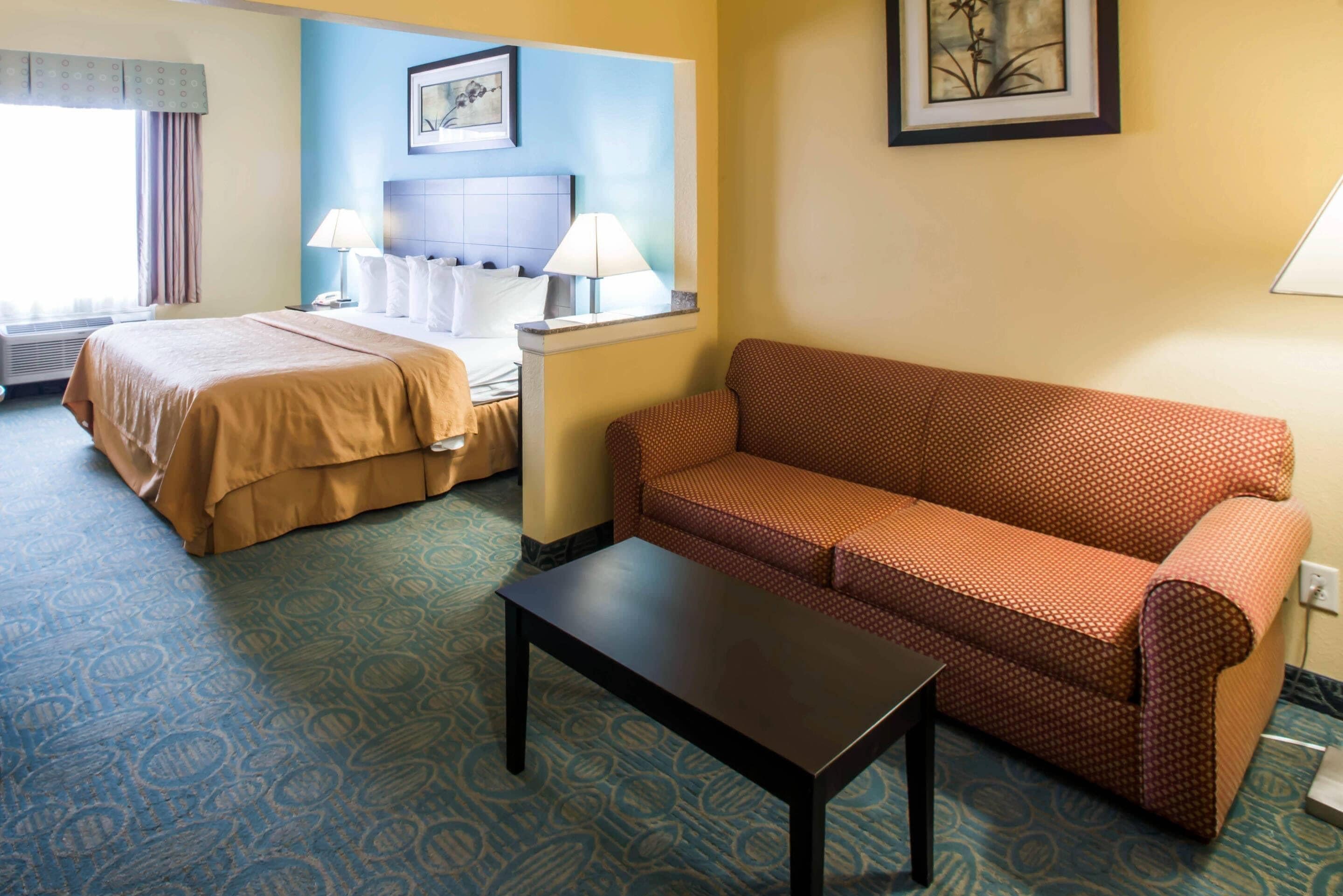 A hotel room with a bed, a sofa, a table, and two lamps.