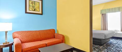 Een hotelkamer met een blauwe muur, een gele muur, een afbeelding in een lijst, een rode bank, een klein tafeltje en een bed met uitzicht.