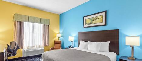 A hotel room with a bed, two bedside lamps, a chair, a desk with a computer, and a window with curtains.