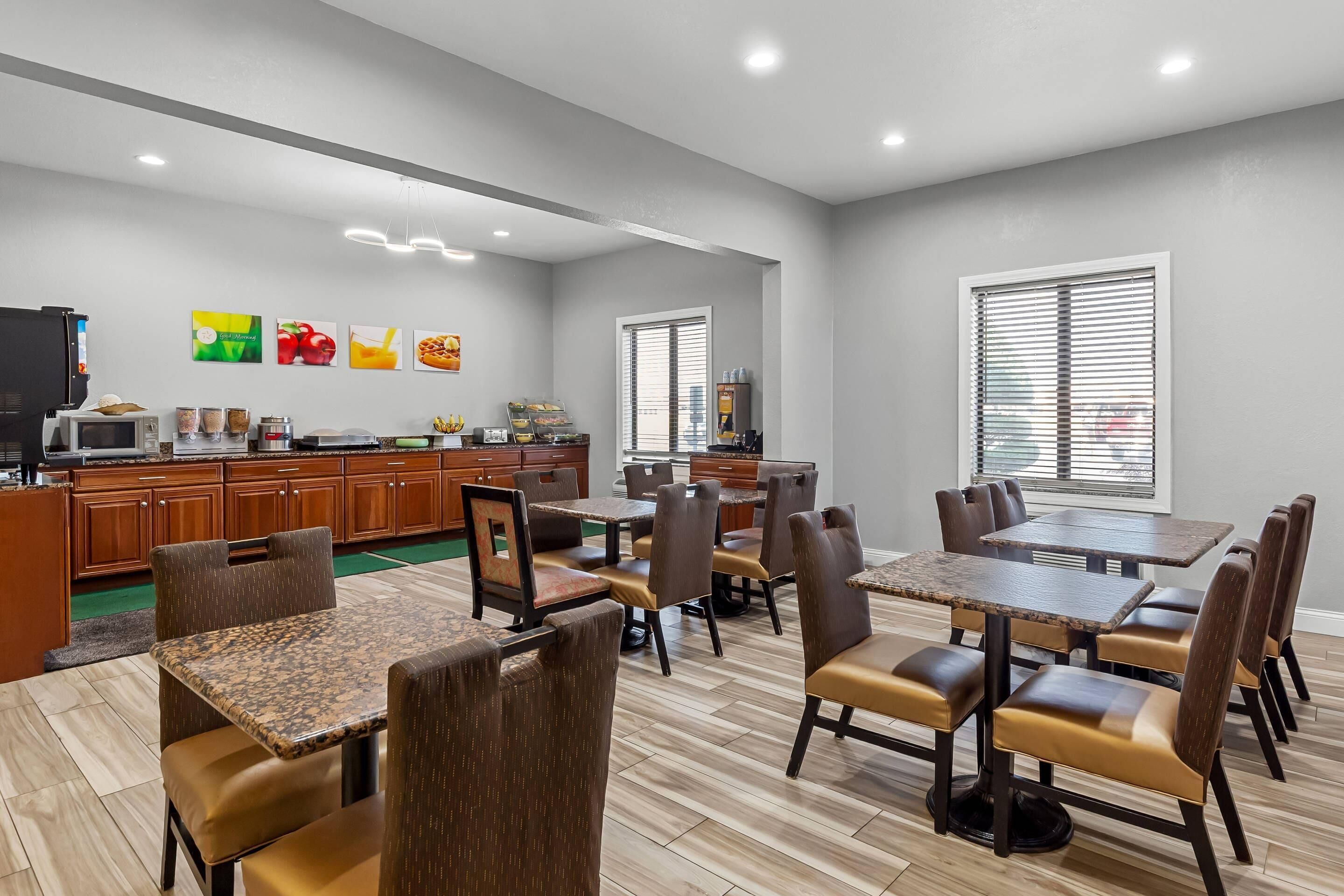A modern dining area with multiple tables and chairs, a kitchen area with appliances, and artwork on the walls.