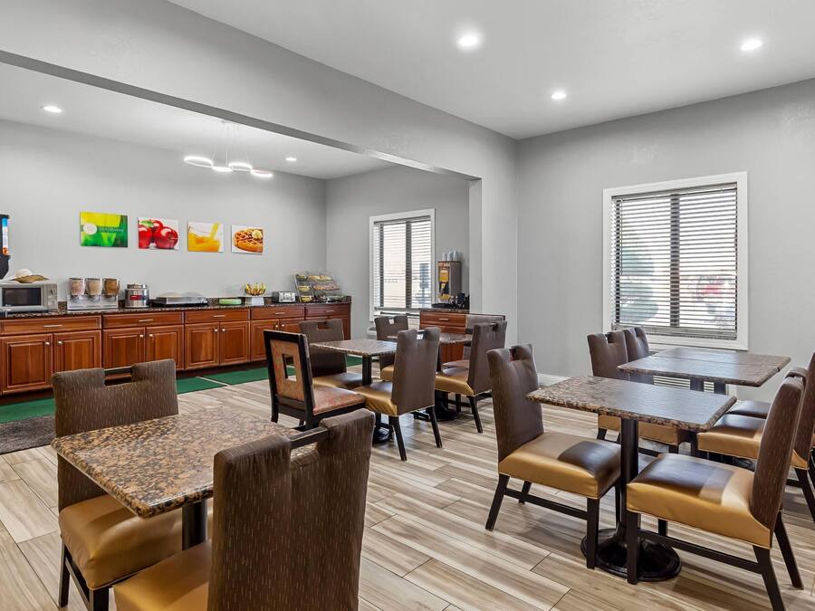 A modern dining area with multiple tables and chairs, a kitchen area with appliances, and artwork on the walls.