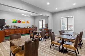 A modern dining area with multiple tables and chairs, a kitchen area with appliances, and artwork on the walls.
