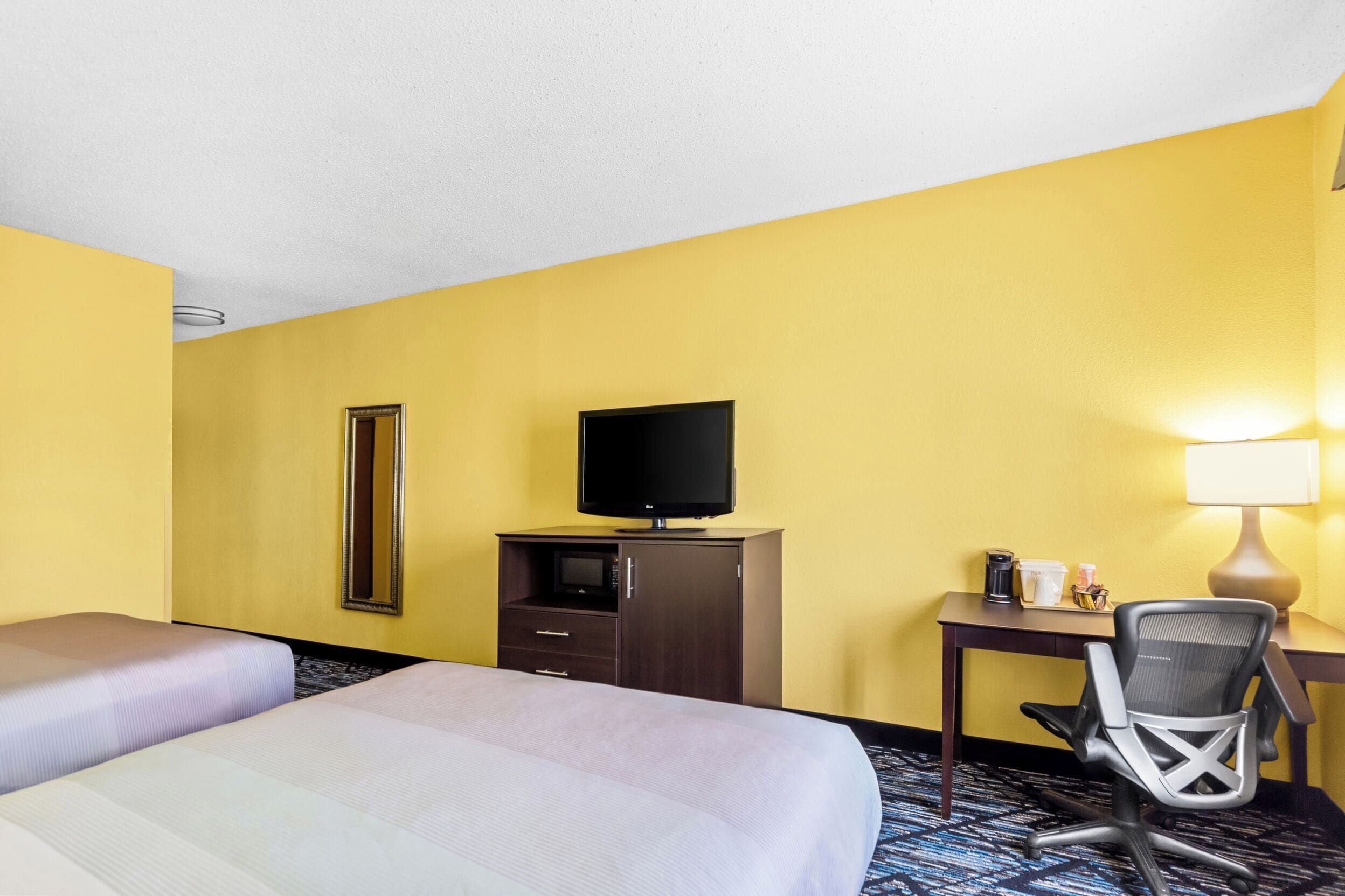 Una camera d'albergo con due letti, una scrivania con una sedia, una televisione e una lampada.