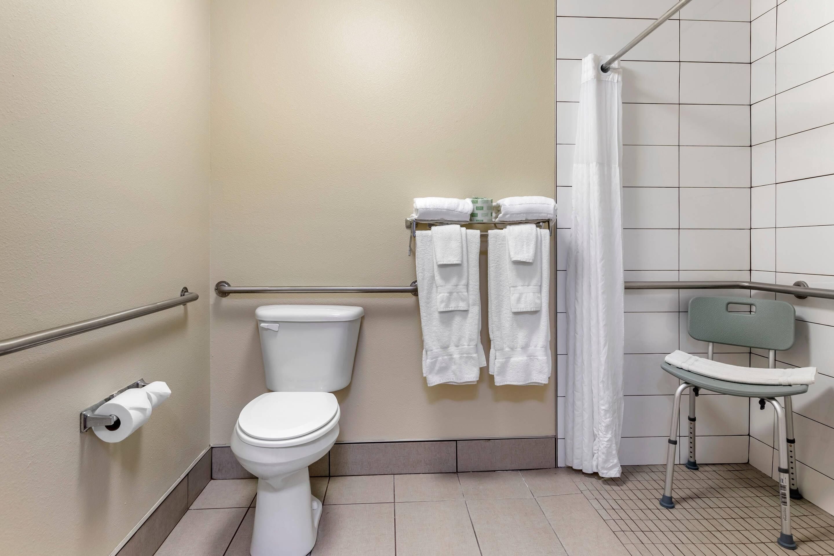 A bathroom with a toilet, a handrail, a shower curtain, and a wheelchair.