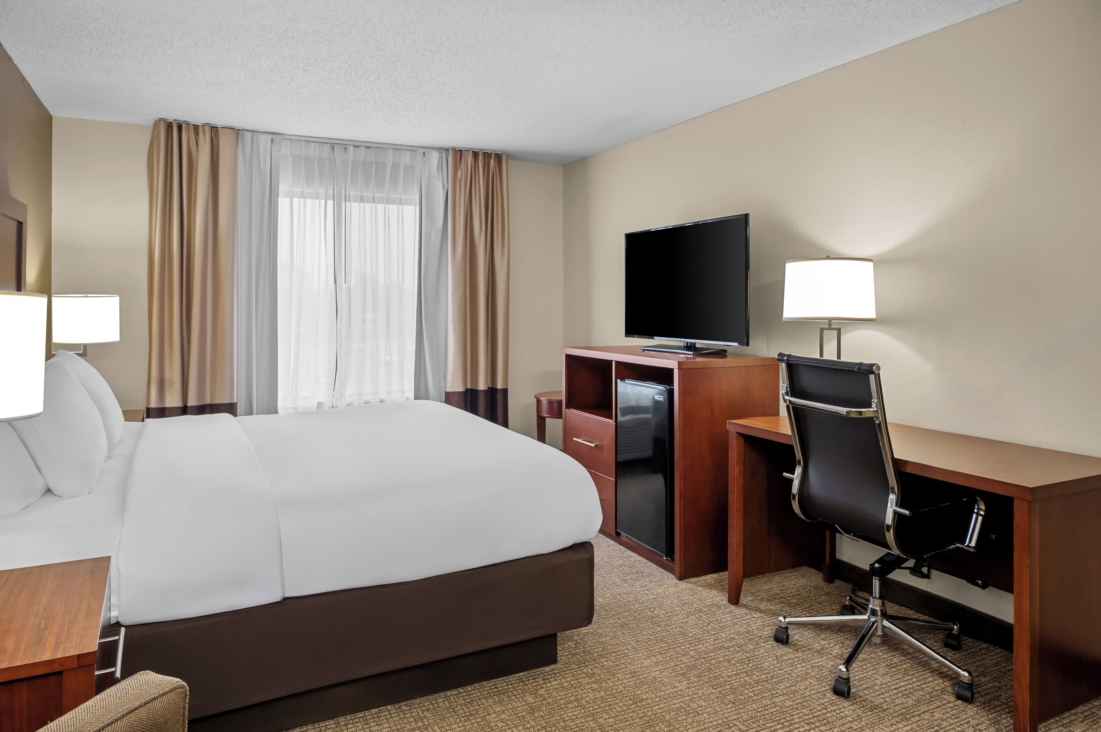 A hotel room with a large bed, a desk with a computer, a TV, and two lamps.