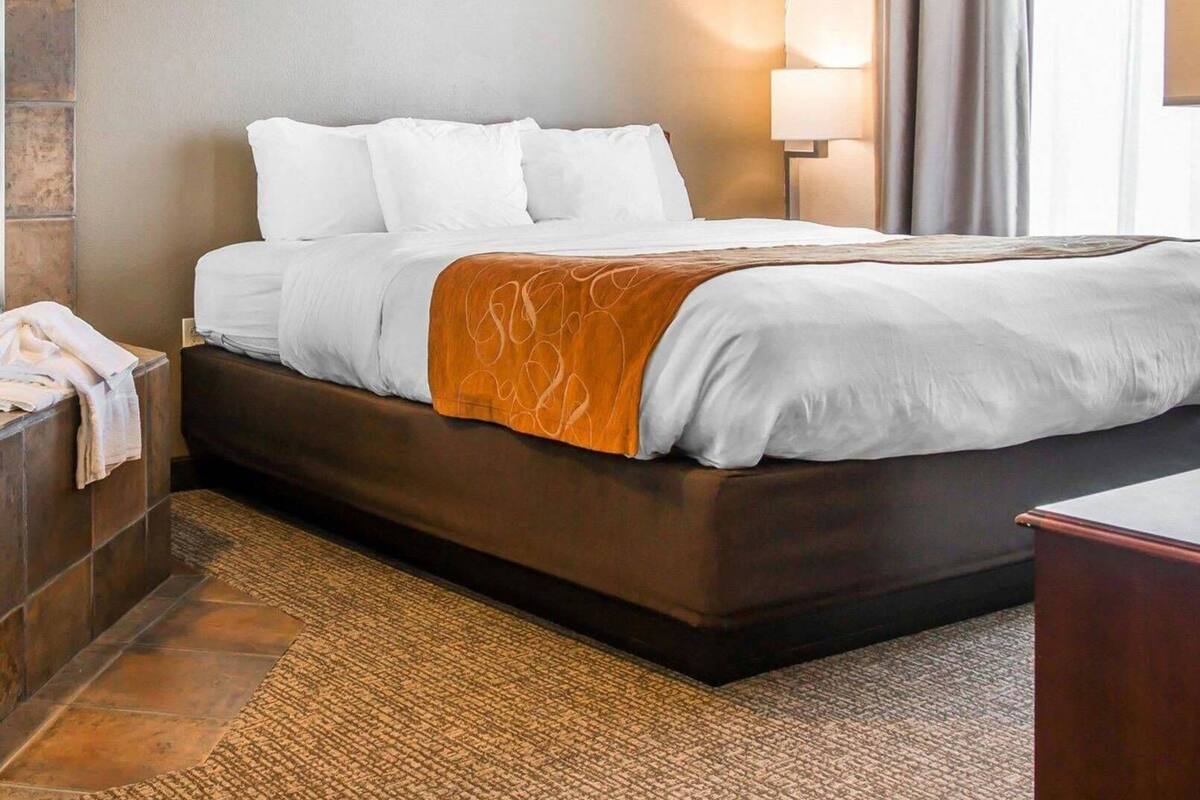 Una habitación de hotel con una cama, una mesita de noche, una lámpara y un ventanal con cortinas.