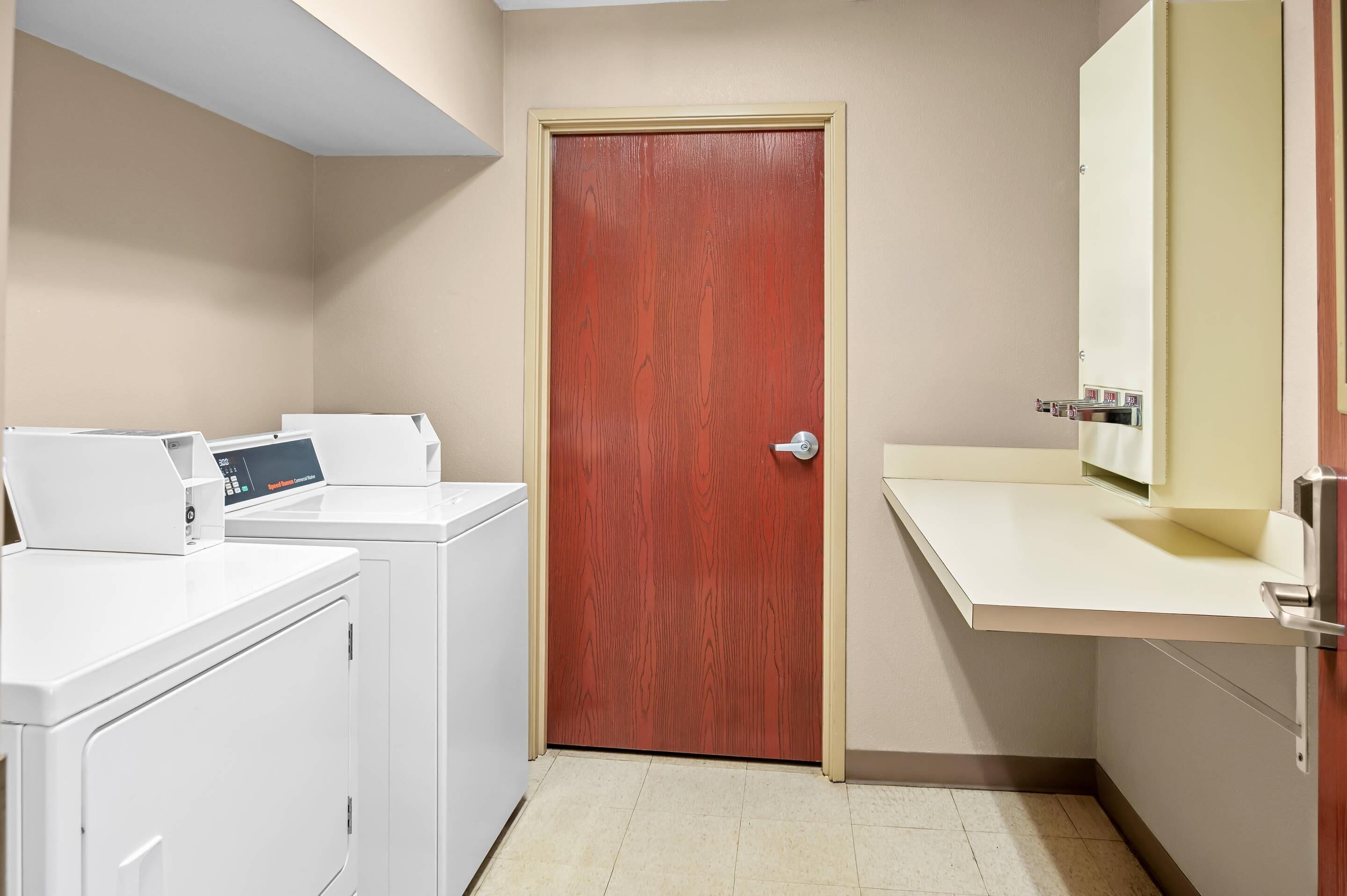 A laundry room with a wooden door, a washing machine, and a countertop with a sink.