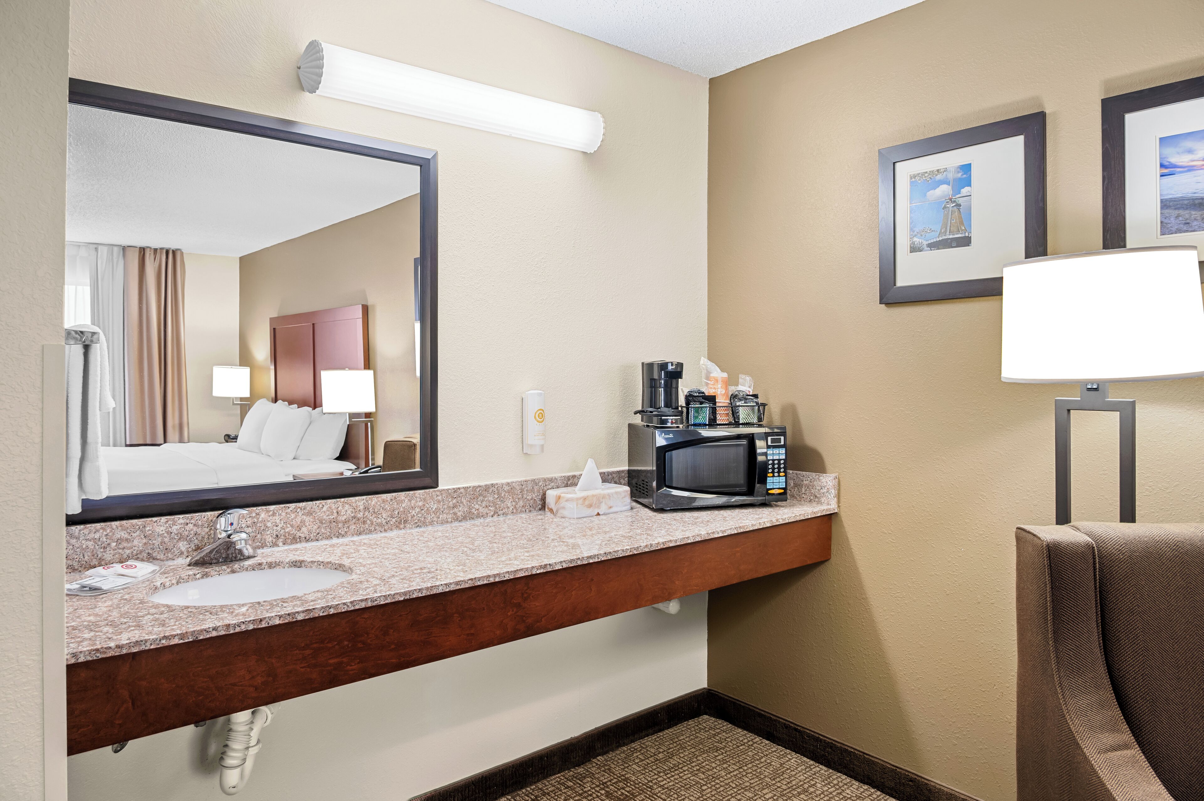 A hotel bathroom with a large mirror, a sink, a coffee maker, and a towel dispenser.