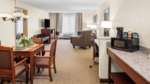 Habitación de hotel con comedor, sofá, televisor, microondas y cafetera.