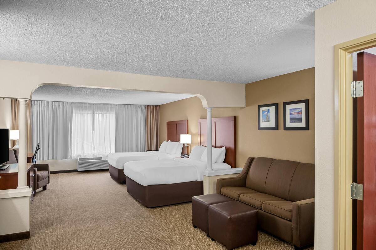 Una habitación de hotel con dos camas, un escritorio, una silla, un sofá y un televisor.