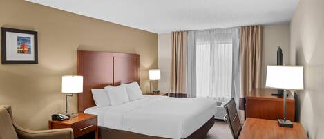 A hotel room with a large bed, two bedside tables with lamps, a chair, a desk, and a picture on the wall.