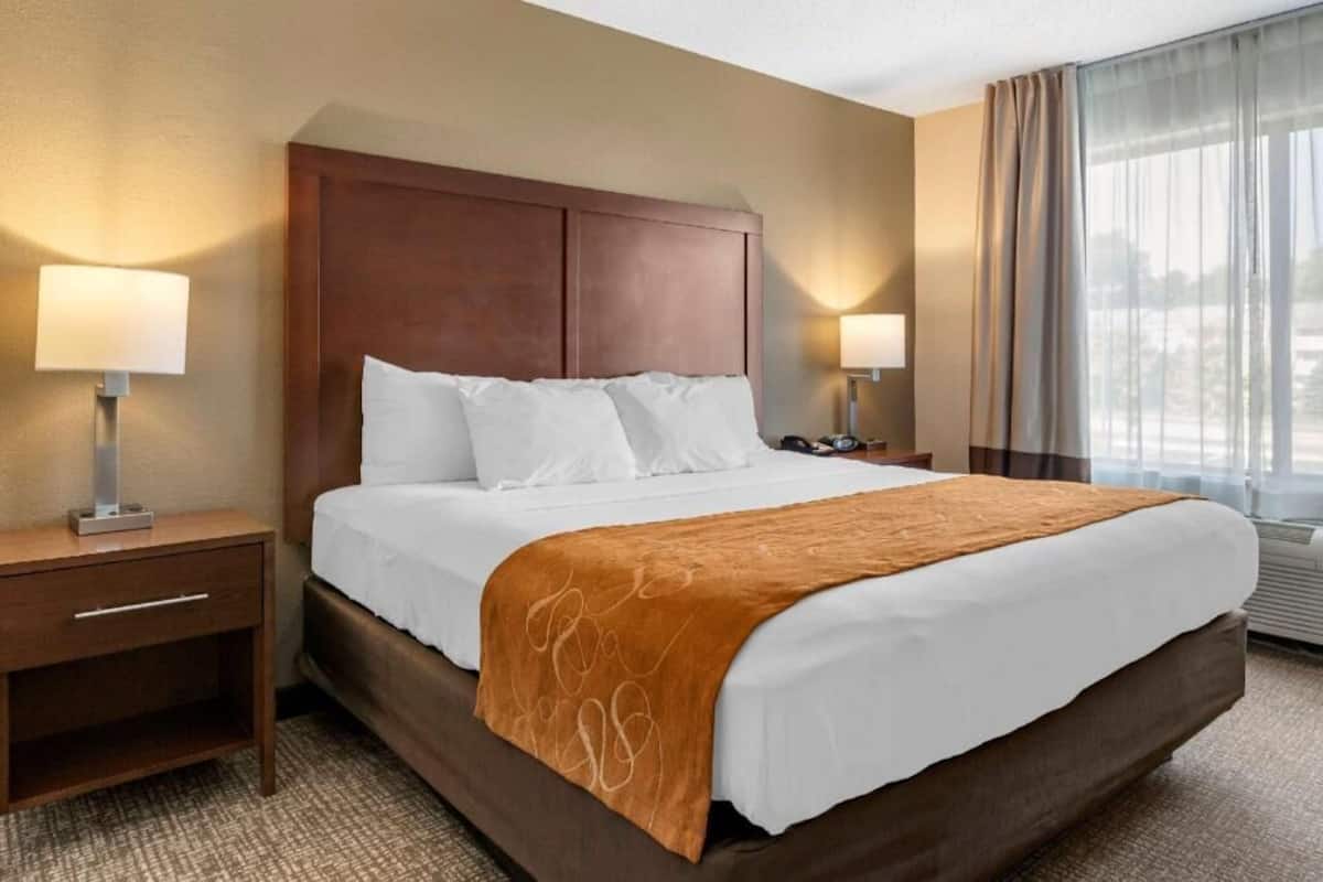 Habitación de hotel con una cama grande, dos mesitas de noche, una ventana con cortinas y vistas a la ciudad.