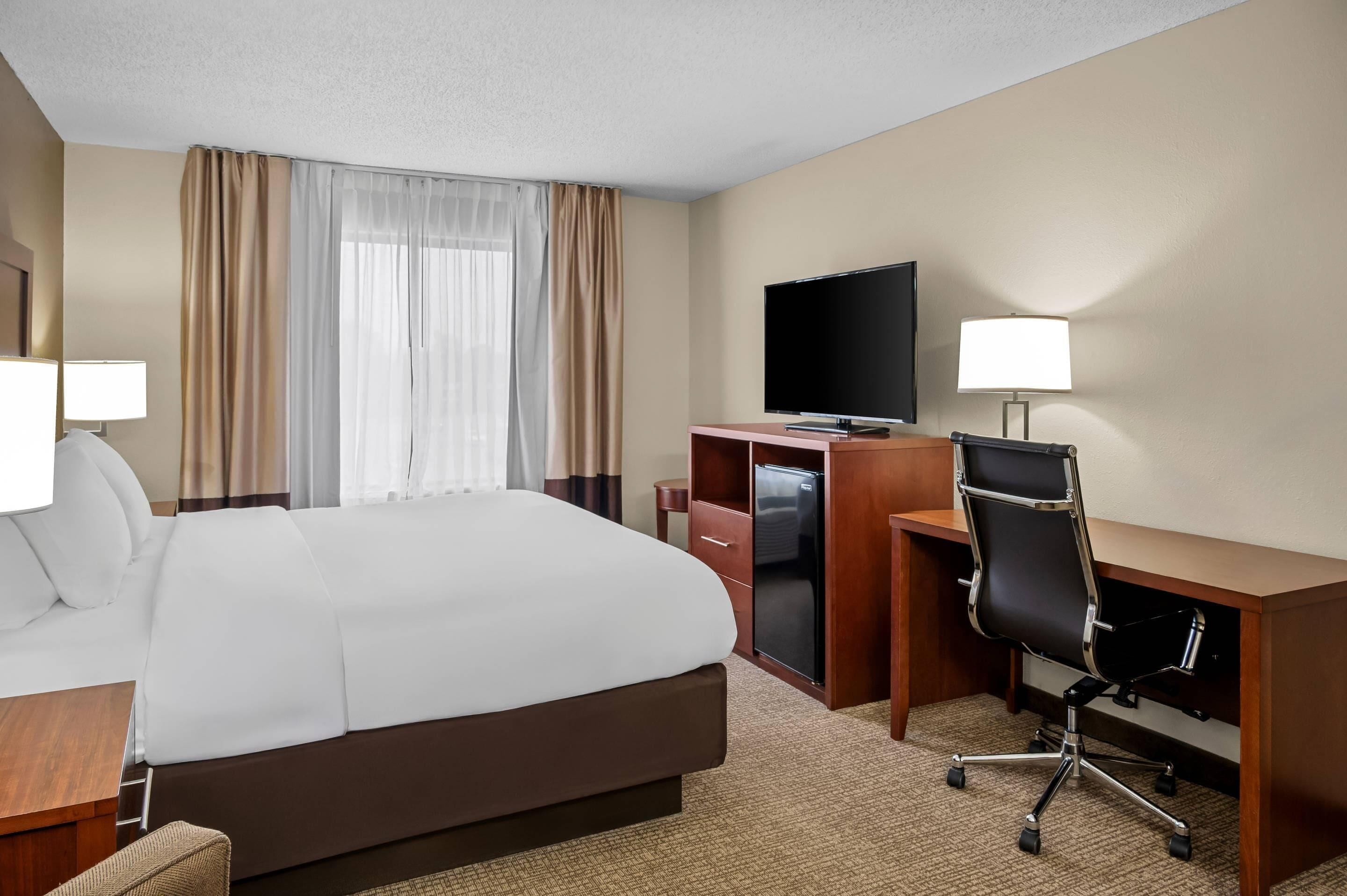 A hotel room with a large bed, a desk with a computer, a TV, and a chair.