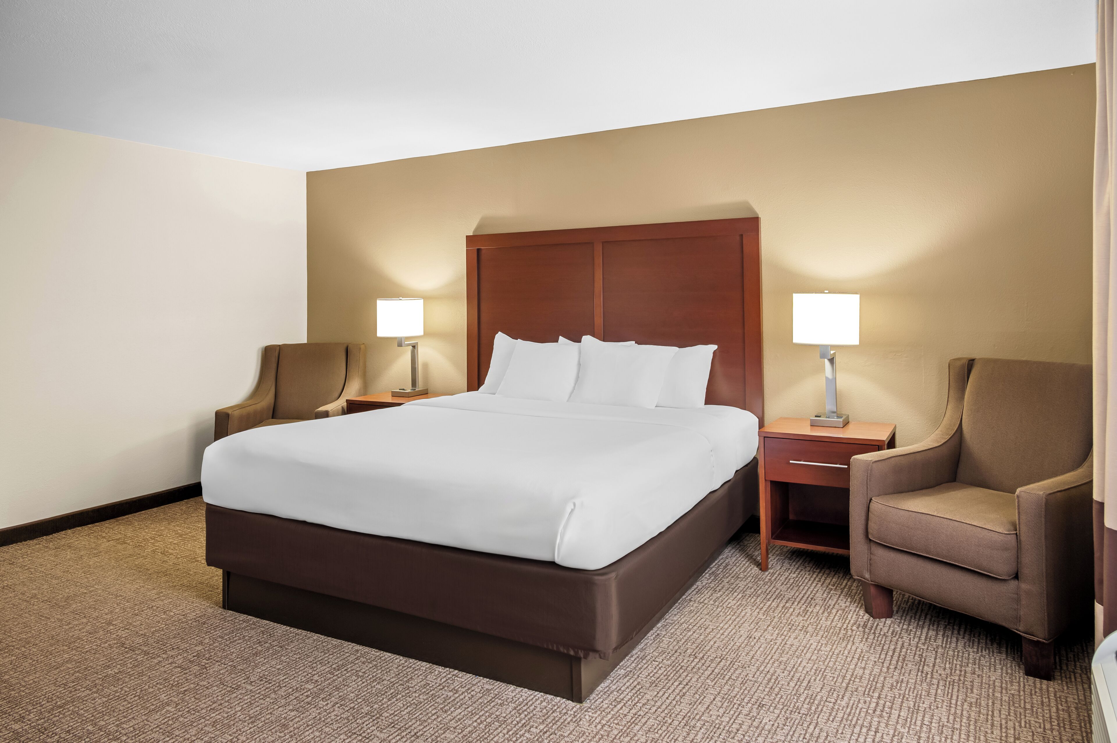 Una habitación de hotel con una cama grande, dos mesitas de noche, dos lámparas y dos sillones.