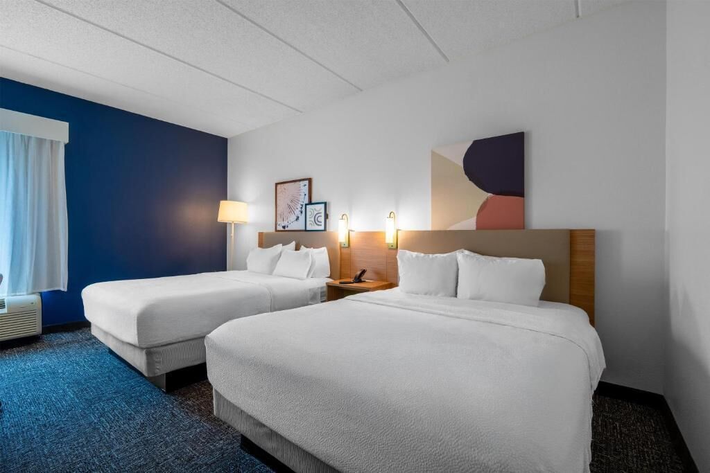 A hotel room with two beds, a nightstand, a lamp, and a framed picture on the wall.