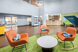 Eine moderne Hotelhalle mit einer Rezeption, einer Lounge mit Schaukelstühlen, einem durch Glastüren einsehbaren Poolbereich und einem Automaten.