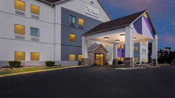 A hotel with a modern design, featuring a prominent 'spark by Hilton' sign, a covered entrance, and multiple windows with illuminated interiors.