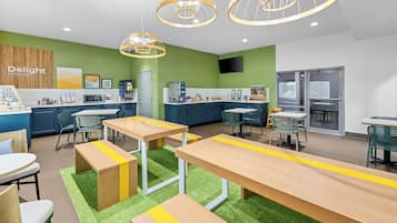 Cozinha moderna com paredes verdes, armários de madeira e uma ilha central. Possui diversos espaços com mesas e cadeiras.