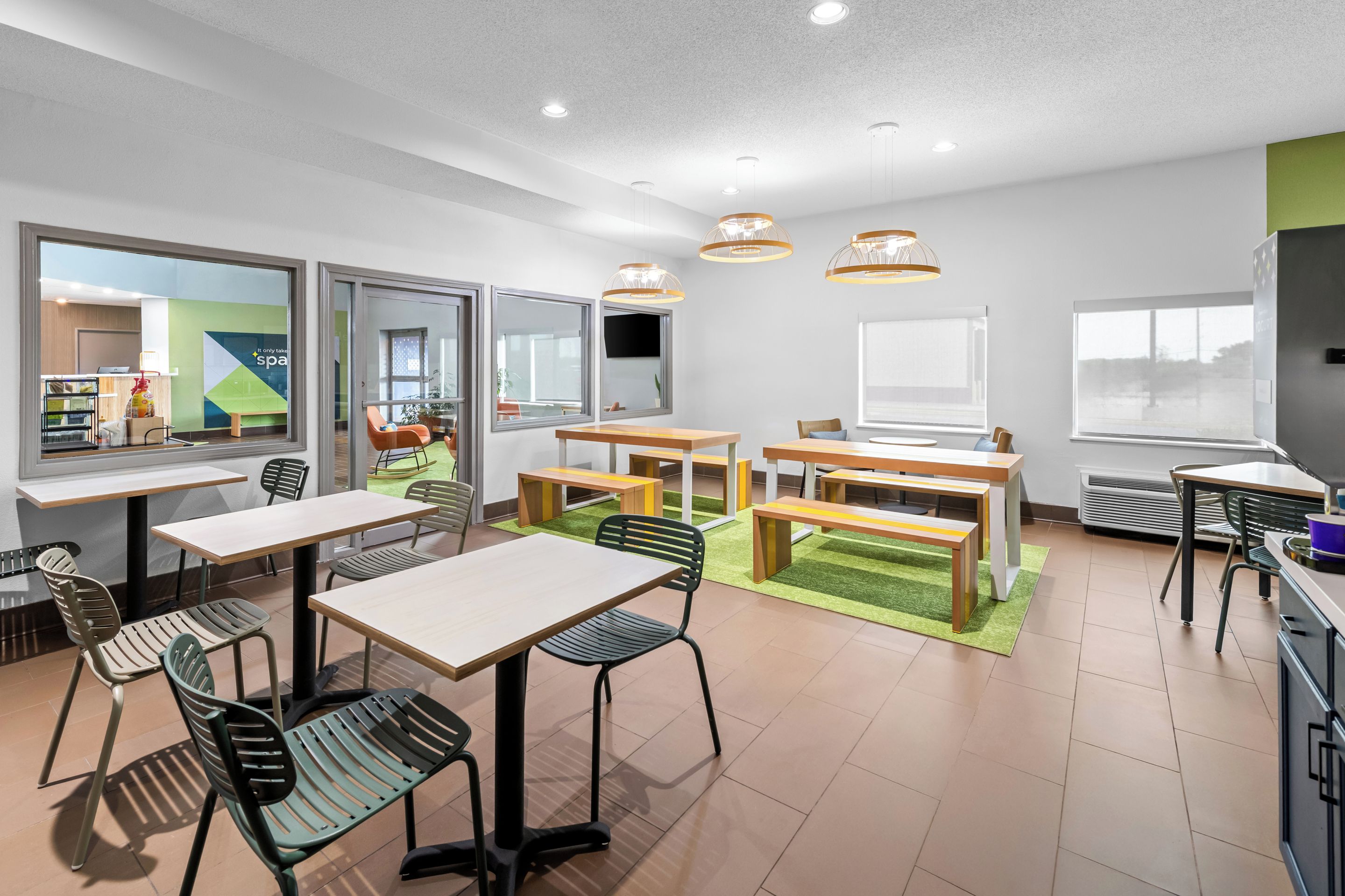 Espaço moderno e interno com várias mesas e cadeiras, grandes janelas e luminárias no teto.