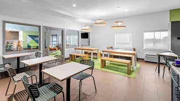 Espaço moderno e interno com várias mesas e cadeiras, grandes janelas e luminárias no teto.