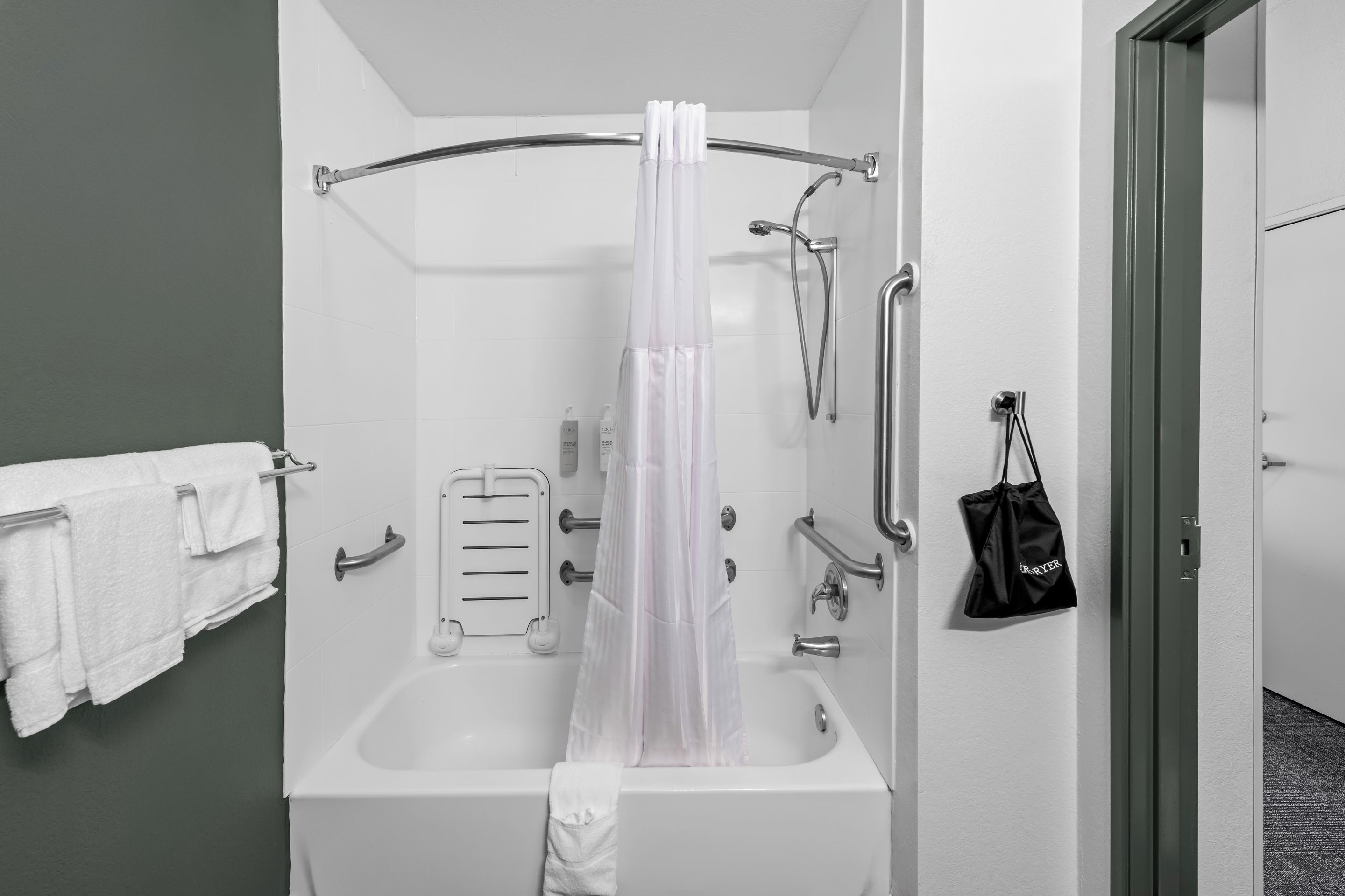 Une salle de bain moderne équipée d’une baignoire, d’une douche et de toilettes. On y trouve également des barres d’appui et un porte-serviettes.
