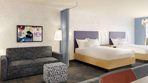 Une chambre d’hôtel avec un canapé, deux lits, un pouf à motifs, une œuvre d’art murale et une fenêtre.