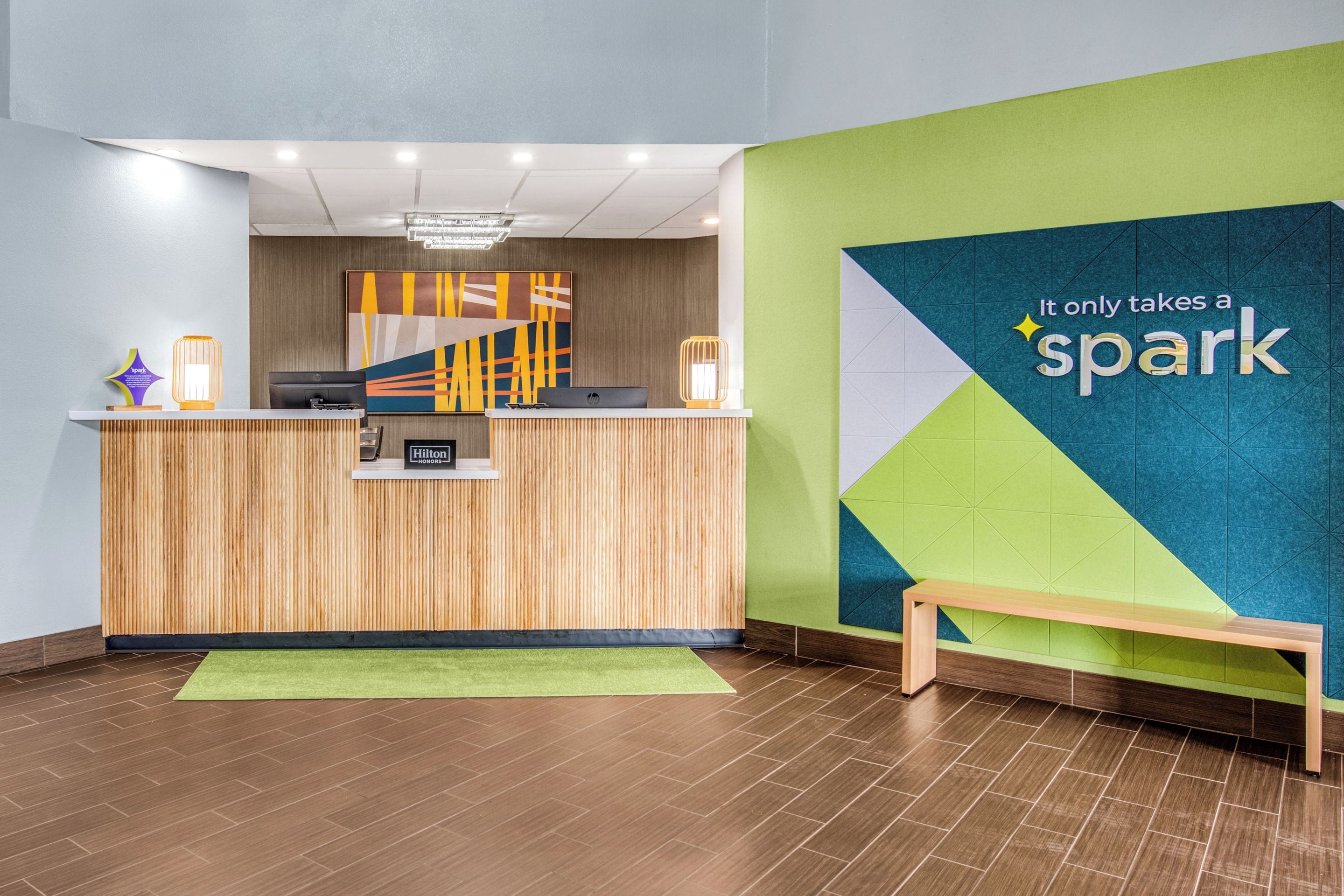 Um balcão de recepção com design moderno, uma parede verde com o letreiro 'spark' e um banco de madeira.